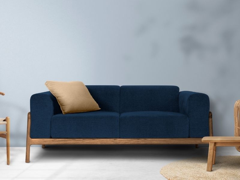 Sofá de dois lugares em tecido azul marinho com estrutura e pés de madeira exposta, sobre um piso claro e fundo azul-acinzentado.