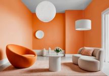 Sala de estar com paredes em laranja pêssego, apresentando uma poltrona esférica laranja escura e um sofá curvo nude/bege, sobre um tapete rosa.