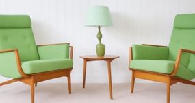 Duas poltronas verdes com mesa lateral em madeira e luminária decorativa.