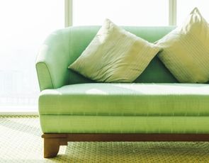 Sofá verde com almofadas decorativas em ambiente iluminado.