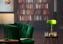 Poltrona verde em ambiente sofisticado com luminária e estante ao fundo.