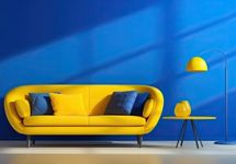 Sofá amarelo curvo com almofadas azuis e amarelas, posicionado contra uma parede azul royal iluminada por luz solar dramática.