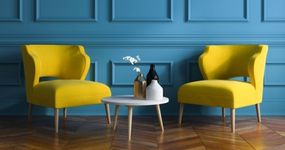 Duas cadeiras estofadas amarelas com design elegante, dispostas simetricamente em frente a uma parede azul petróleo com painéis clássicos.