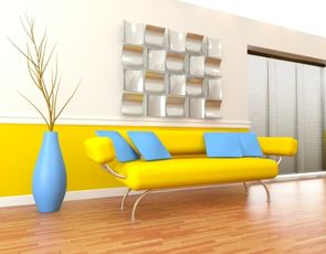 Sofá amarelo moderno com estrutura de metal cromado e almofadas azuis, em uma sala com parede branca e faixa amarela, e um vaso azul grande.